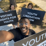 Eric Kennedy, Imogen Gannon, and Susan Milton holding large signs reading Youth Rights, Youth Liberation Now and Voting Rights For Youth respectively, in all caps.